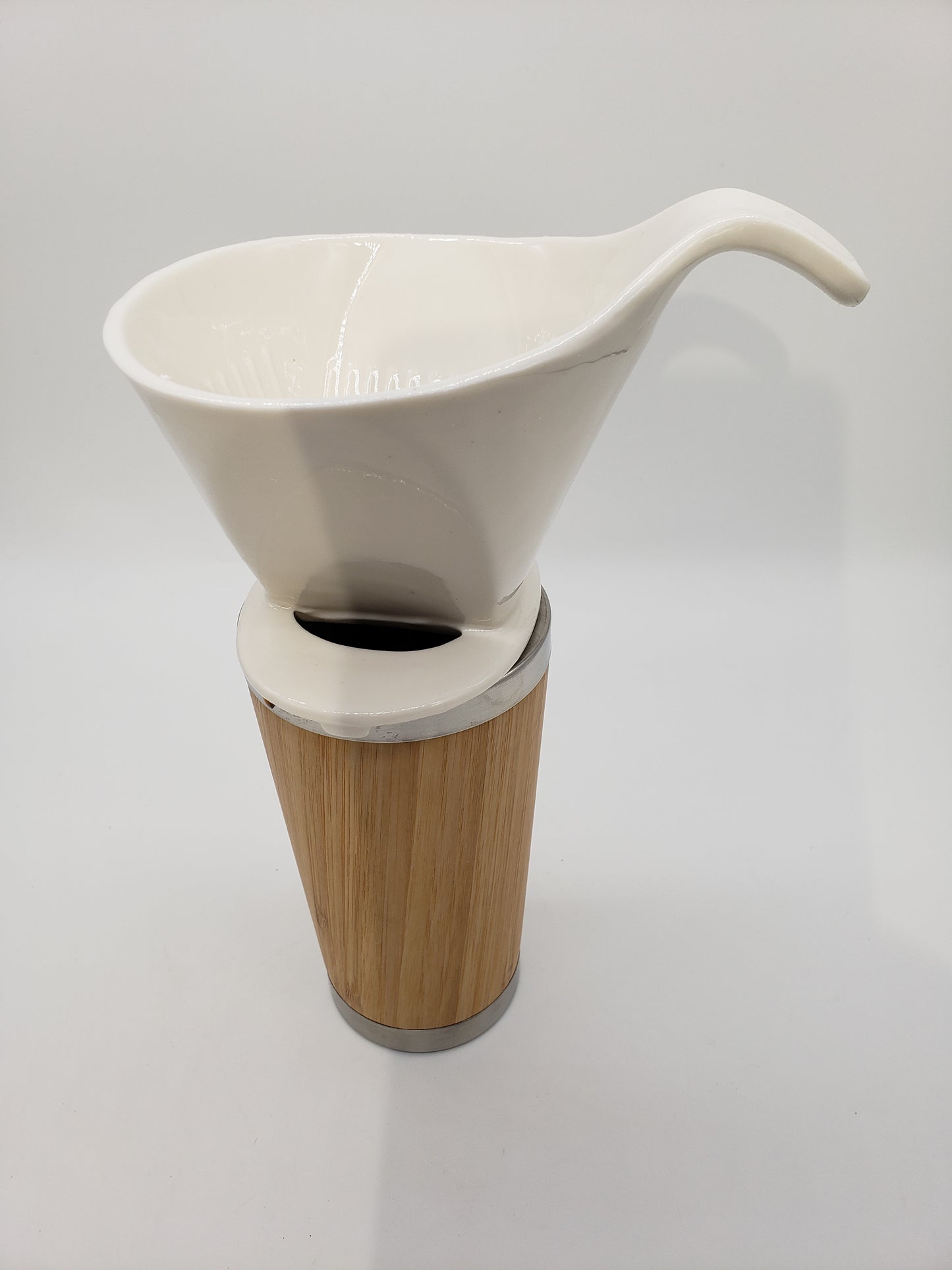 This is a white, shiny, smooth ceramic, cone shaped dripper sitting on top of a bamboo travel mug.  The dripper has an ergonomic handle for an easy grip between finger and thumb.  Insode the dripper is ribbed and three holes are found at the bottom inside for flow performance.  The bottom of the dripper has a base that fits on top of your mug and there is a viewing hole big enough for a finger so you can tell when it is time to stop pouring.   Mug not included.